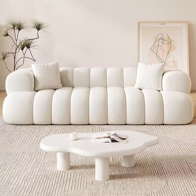 Designed for contemporary living rooms, this plush fabric sofa boasts a sculptural silhouette with deep channel tufting, soft rounded arms, and a low-profile form that suits both cozy homes and statement interiors