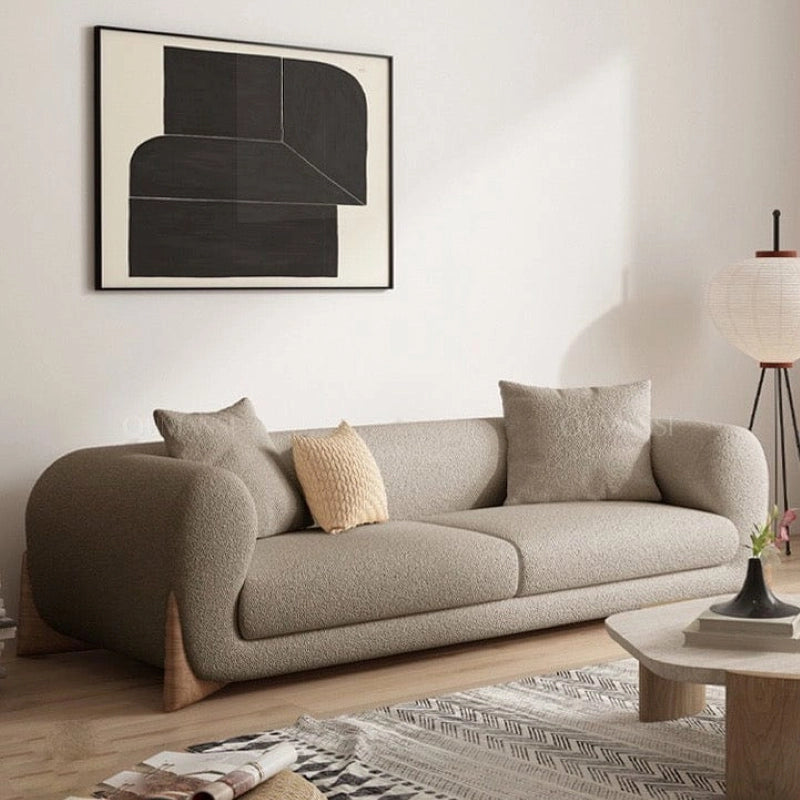 Upholstered in textured bouclé fabric in shades like taupe or ivory, the Boston settee features rounded curves, deep seating, and organically integrated arms for a warm and inviting feel. 