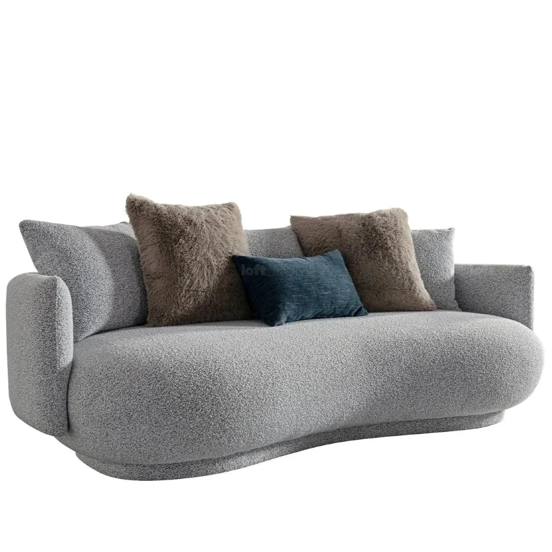Upholstered in textured pebble grey boucle, the design features fixed seat cushions and low sloped arms that form a continuous bean-shaped profile—ideal for compact living spaces