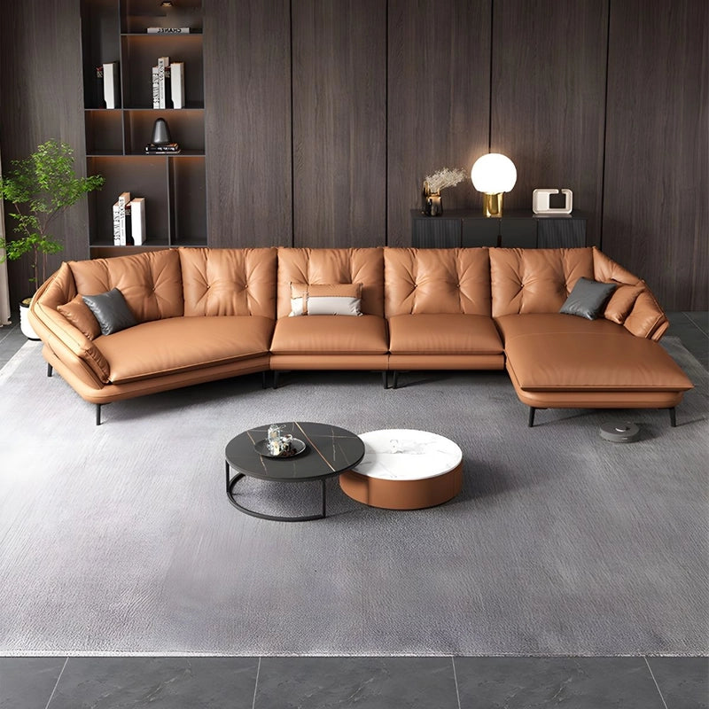 Brown leather sectional L shaped sofa in a modern living room with a gray rug and decorative items.